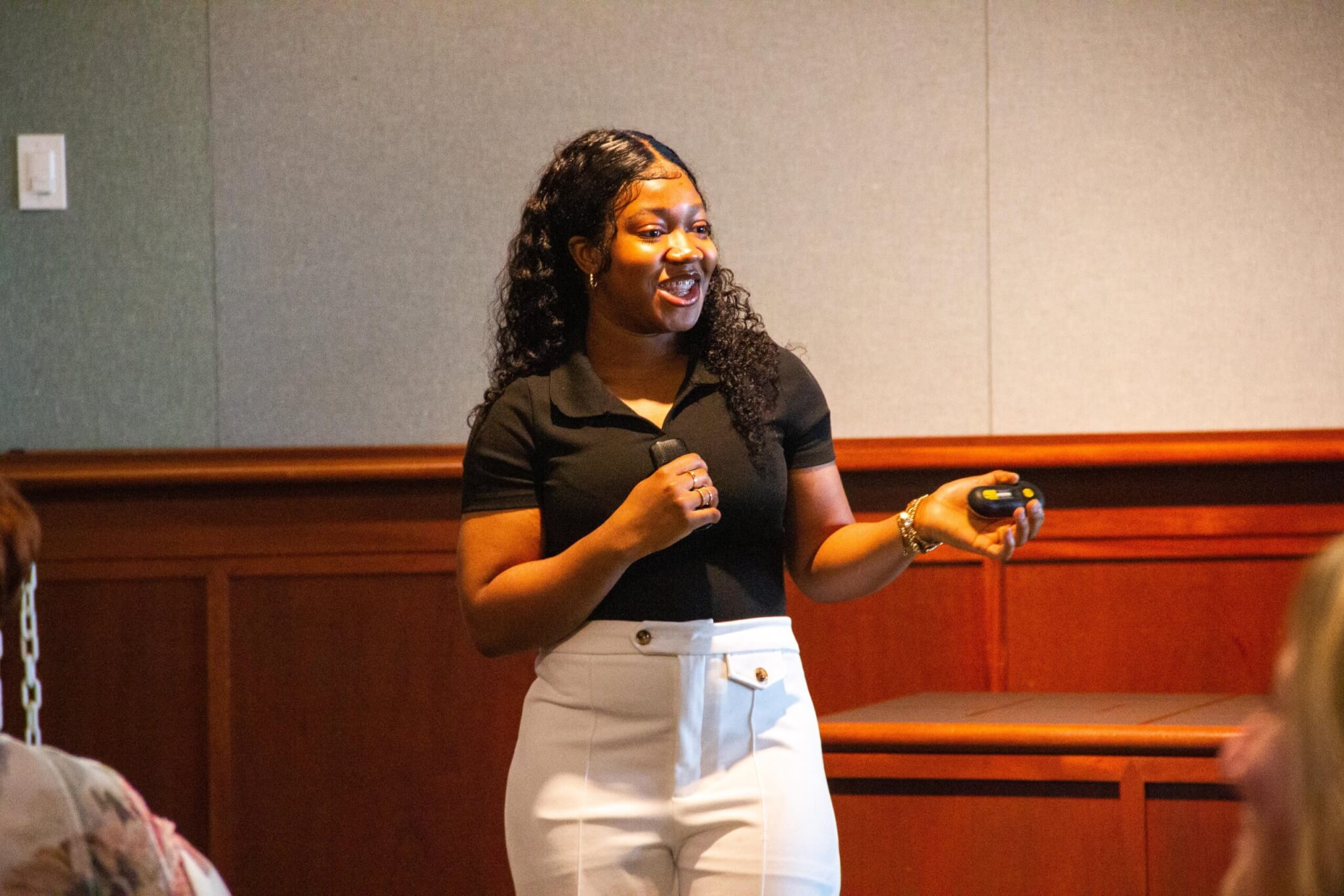 A particiapant in the YEP program standing in front of other attendees sharing a story while she gestures and holds a PowerPoint controller.