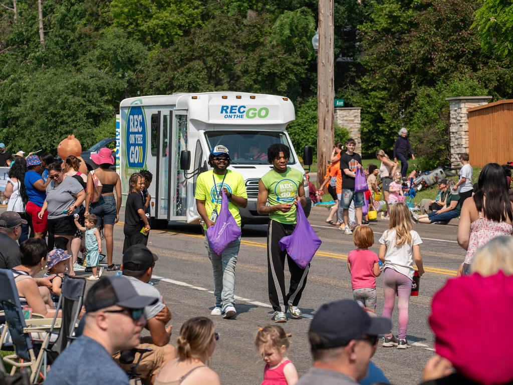 Youth walking in a parade handing out candy to people on the sidewalk