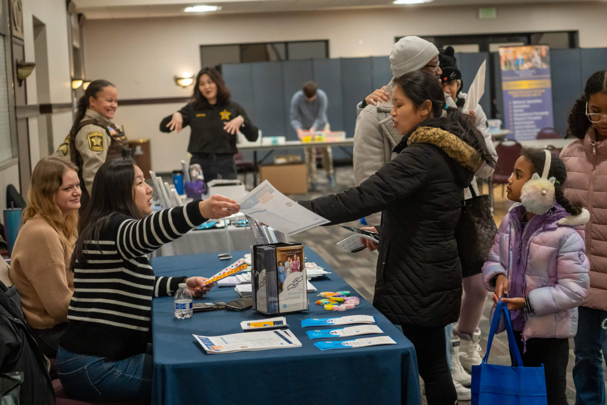 Person handing another person a piece of paper full of resources. People in the background at a resource fair.