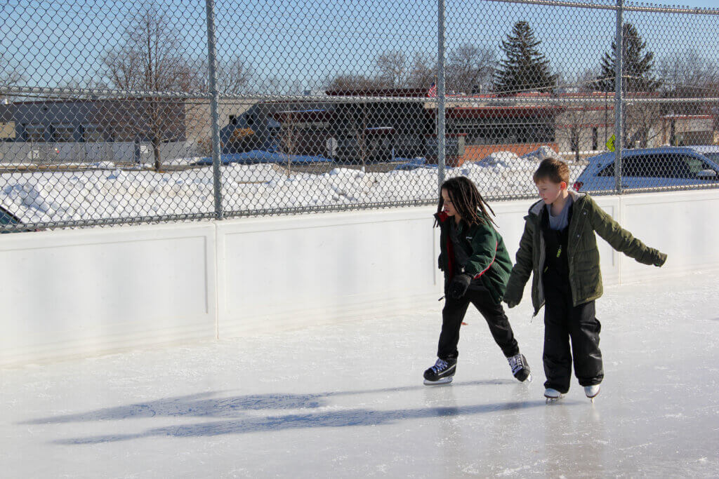 Two kids skating on an outdoor ice rink