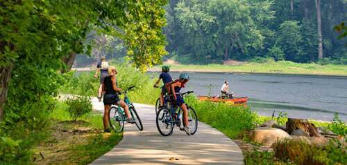 Three people on bikes with a river in the background including someone on a boat