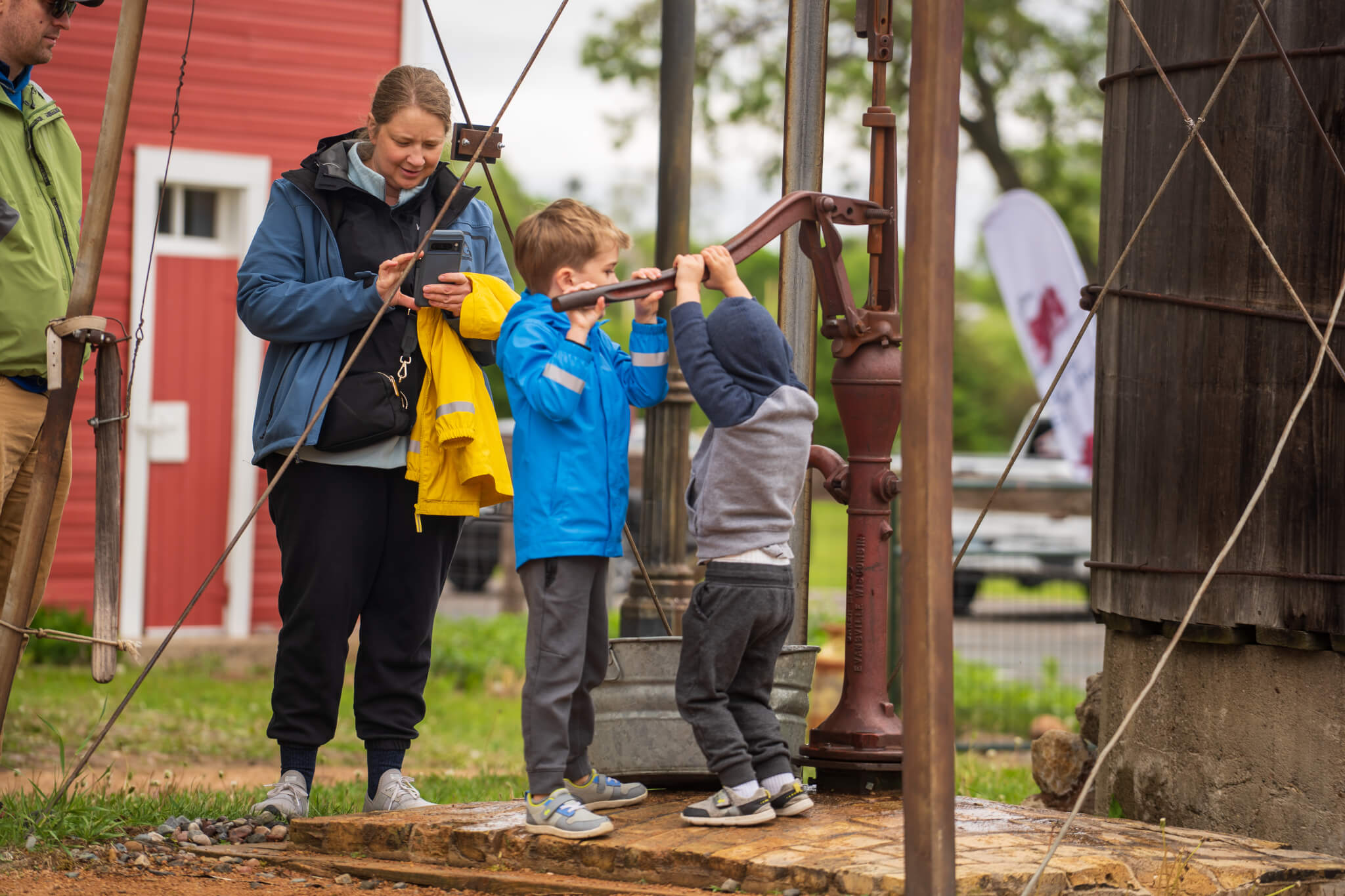 Kids playing with a water well pump, adult in background
